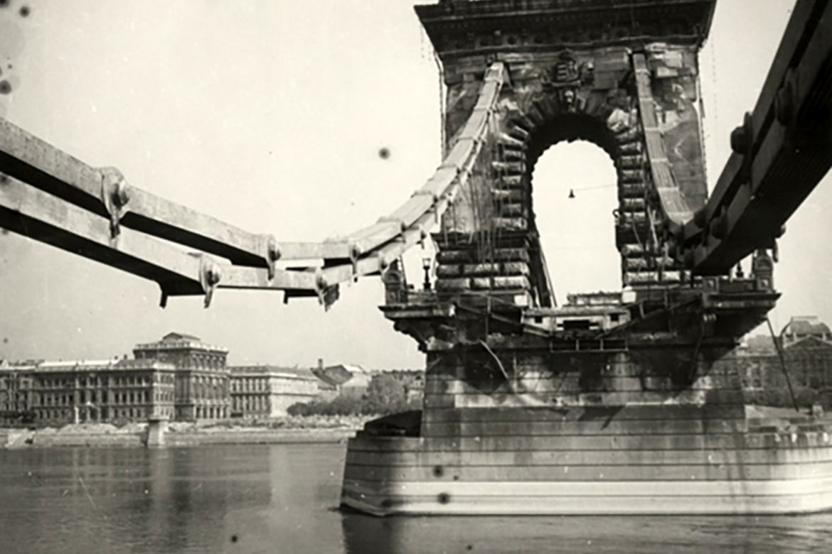 A Lánchíd roncsai Budáról fotózva, a háttérben a Magyar Tudományos Akadémia épülete és a Gresham palota. Forrás: Nullaév / MNM Fotótár